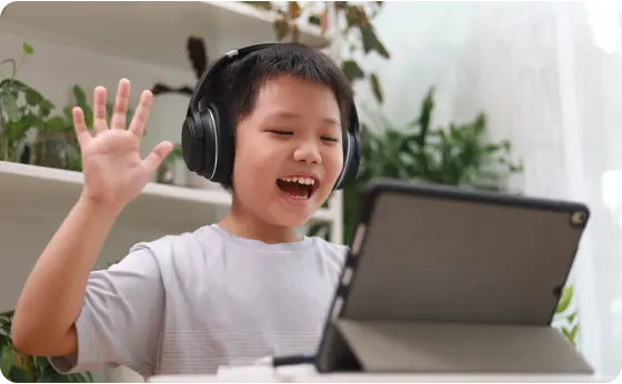 Elementary stuent waiving at his online class and wearing a headset